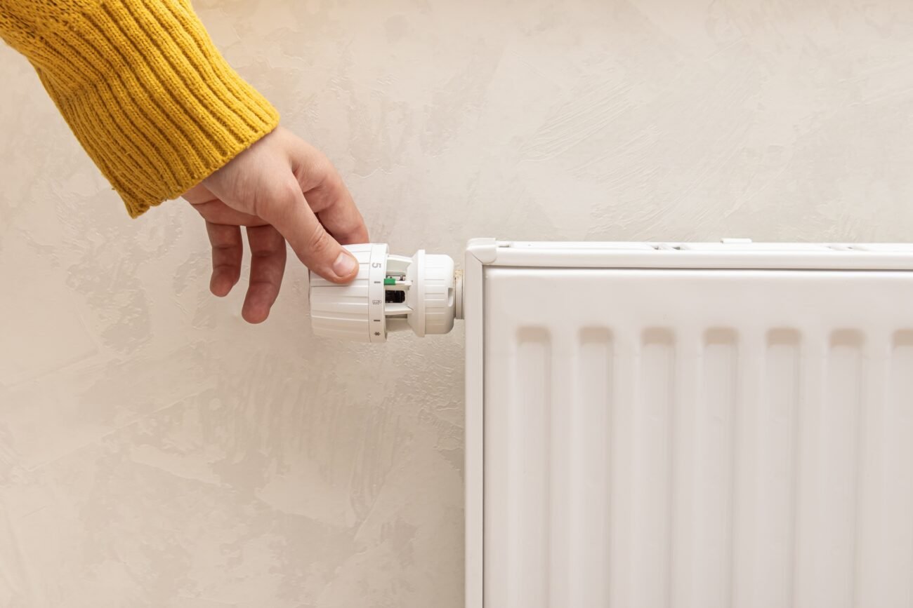 Ranka geltonu megztiniu reguliuoja balto radiatoriaus termostatą