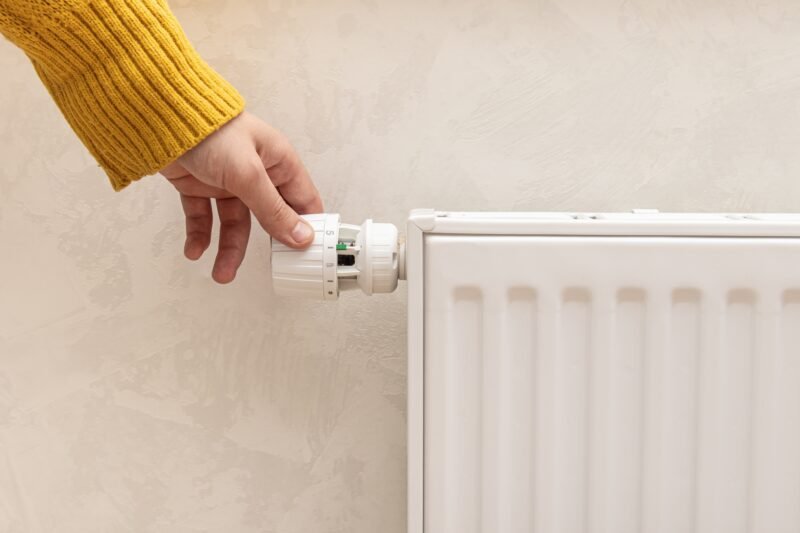 Ranka geltonu megztiniu reguliuoja balto radiatoriaus termostatą