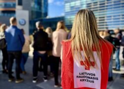 Lietuvos Raudonojo Kryžiaus savanorė raudona liemene stovi žmonių minioje