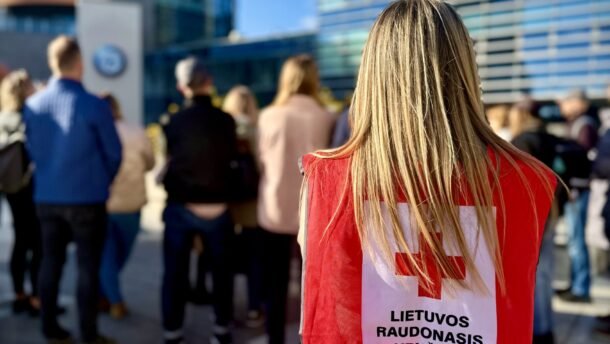Lietuvos Raudonojo Kryžiaus savanorė raudona liemene stovi žmonių minioje