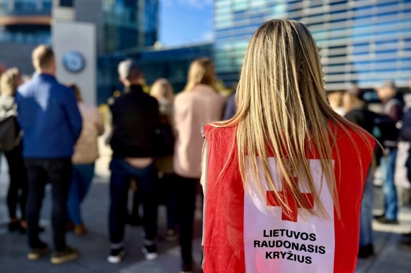 Lietuvos Raudonojo Kryžiaus savanorė raudona liemene stovi žmonių minioje
