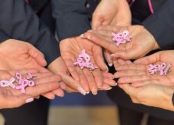 Žmonių rankose laikomi rožiniai kaspinėliai