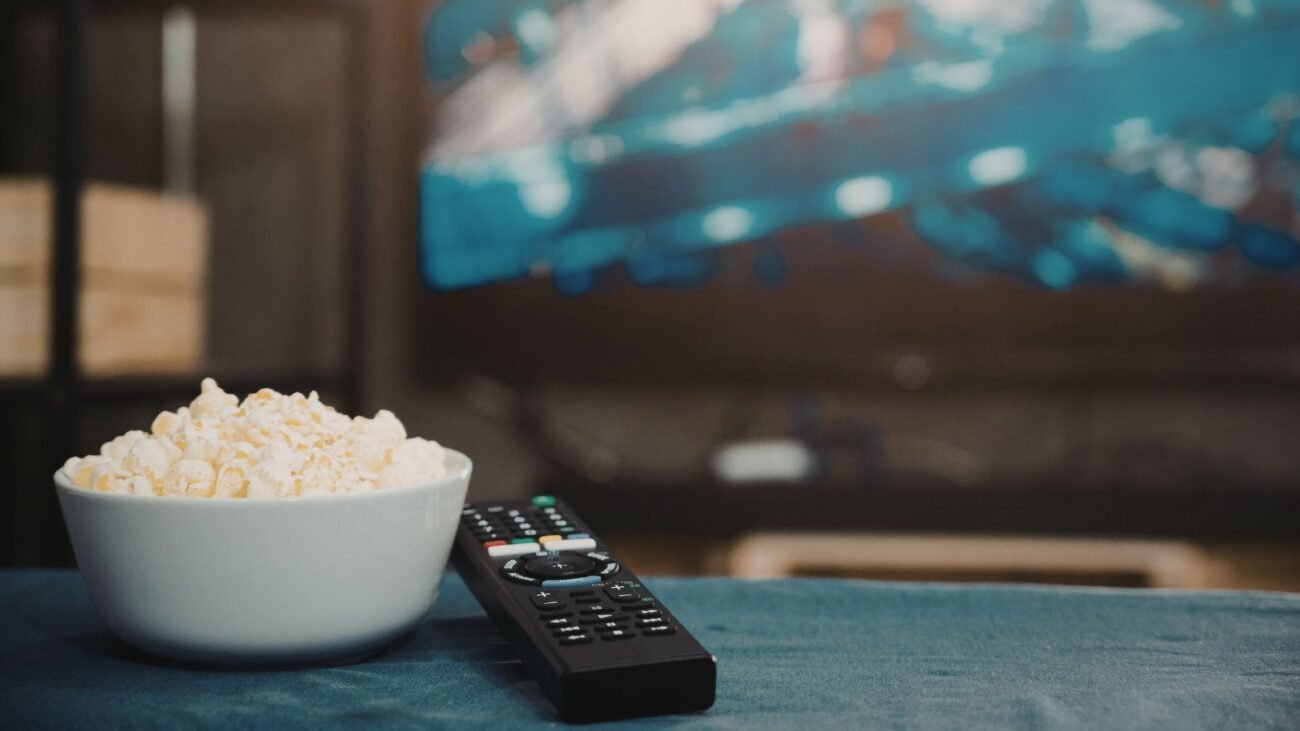 Spragėsių dubuo ir televizoriaus nuotolinio valdymo pultelis prie įjungto televizoriaus
