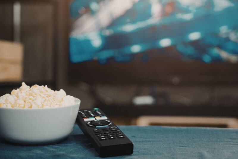Spragėsių dubuo ir televizoriaus nuotolinio valdymo pultelis prie įjungto televizoriaus