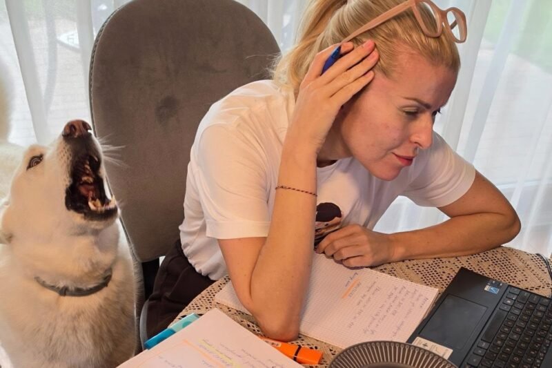 Moteris prie stalo mokosi, o šalia jos sėdi šuo