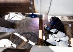 Darbuotojas apsauginiais drabužiais dirba prie didelio vamzdyno