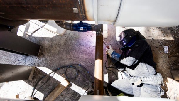Darbuotojas apsauginiais drabužiais dirba prie didelio vamzdyno