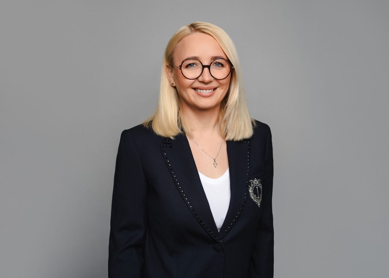 Besijuokianti šviesiaplaukė moteris su akiniais ir tamsiu švarku