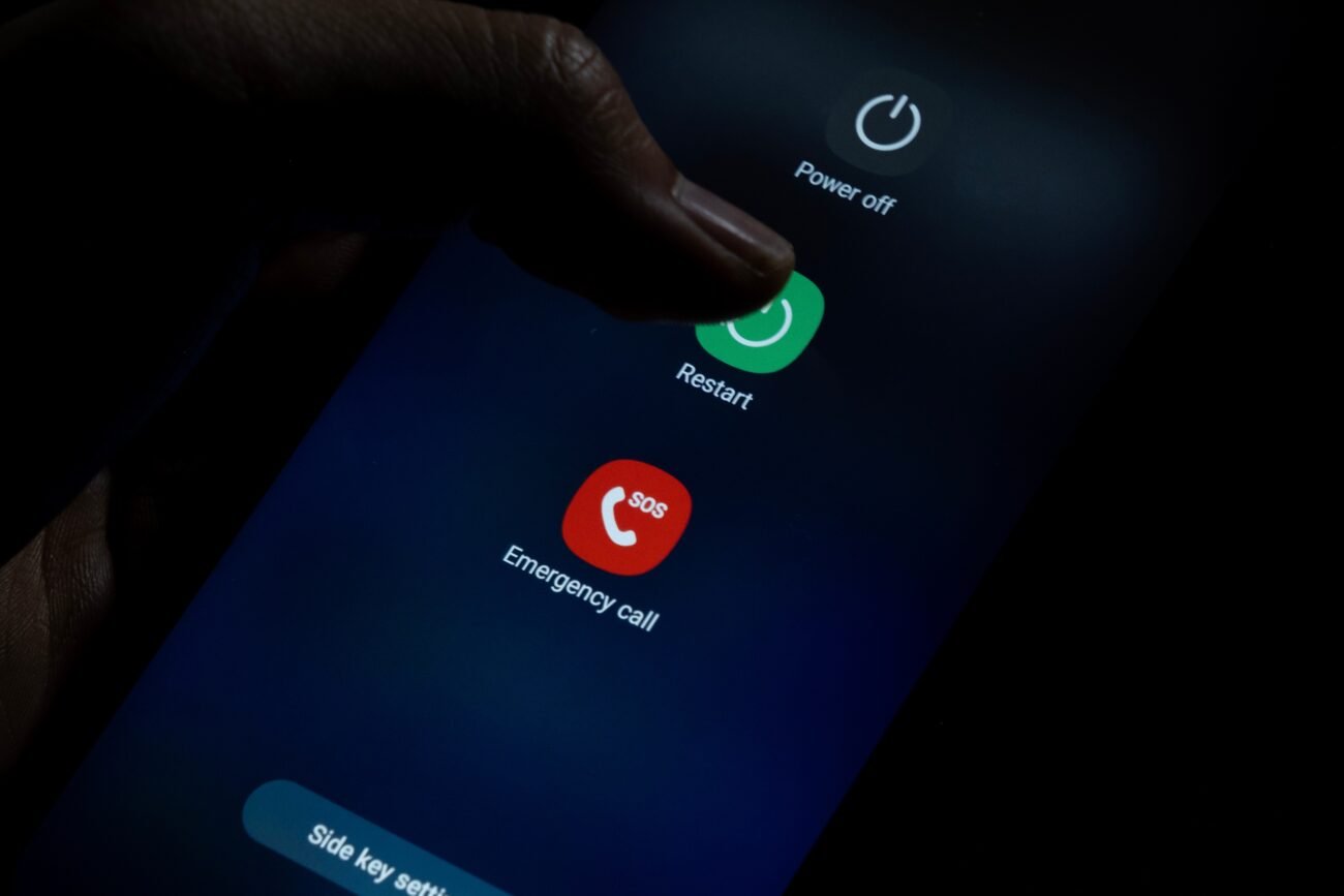 Išmaniojo telefono ekrane atvertas perkrovimo meniu, pirštas liečia mygtuką „Restart“