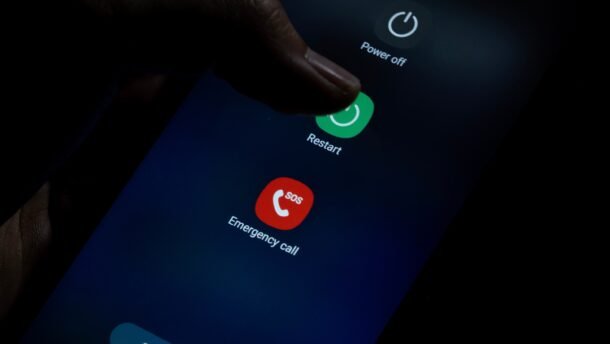 Išmaniojo telefono ekrane atvertas perkrovimo meniu, pirštas liečia mygtuką „Restart“