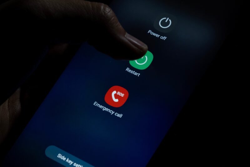 Išmaniojo telefono ekrane atvertas perkrovimo meniu, pirštas liečia mygtuką „Restart“