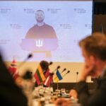 Konferencijos dalyviai stebi Ukrainos atstovo pranešimą dideliame ekrane