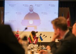 Konferencijos dalyviai stebi Ukrainos atstovo pranešimą dideliame ekrane