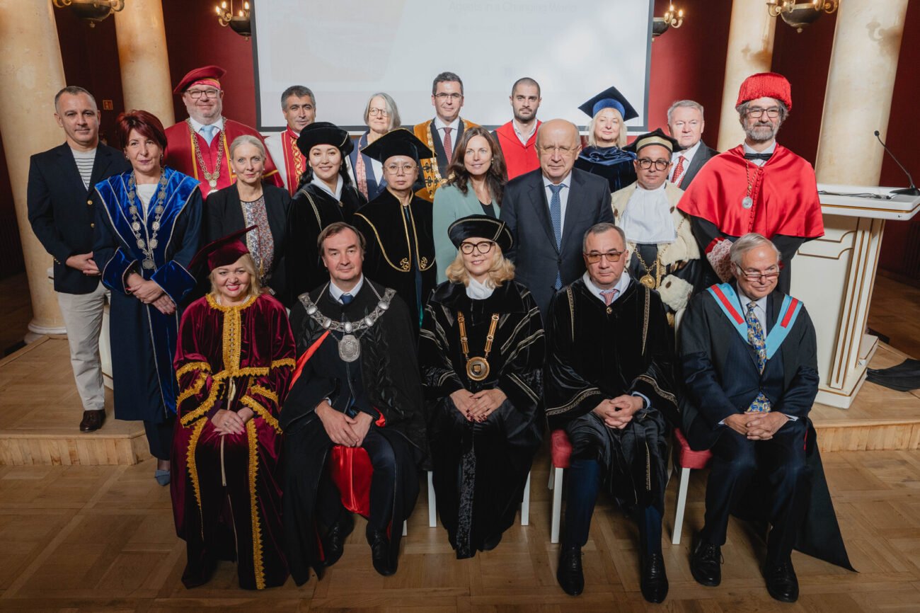 Universitetų atstovai akademiniais drabužiais pozuoja iškilmingoje grupės nuotraukoje