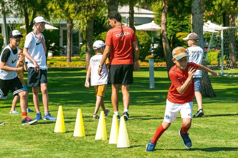 Vaikai lauke treniruojasi su sportiniu kamuoliu, kūgiais ir vikrumo lazdelėmis