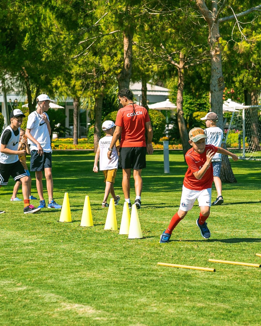 Vaikai lauke treniruojasi su sportiniu kamuoliu, kūgiais ir vikrumo lazdelėmis