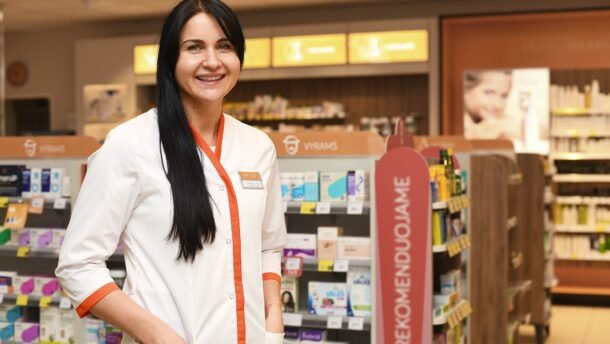 Besišypsanti vaistininkė stovi vaistinės prekybos salėje
