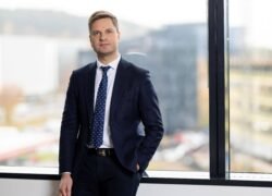 Verslininkas su kostiumu stovi prie didelio biuro lango