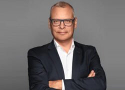 Verslininkas su akiniais ir sukryžiuotomis rankomis vilki tamsų kostiumą