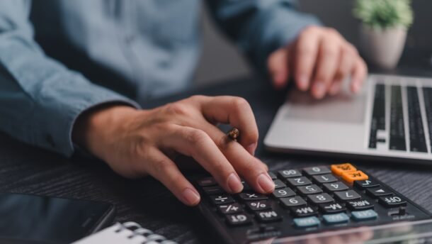 Verslininkas skaičiuoja finansus kalkuliatoriumi prie nešiojamojo kompiuterio