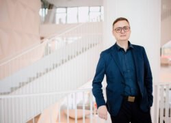 Vyras su akiniais stovi moderniame biure prie laiptų