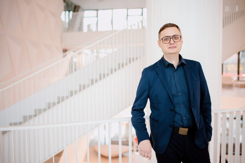 Vyras su akiniais stovi moderniame biure prie laiptų