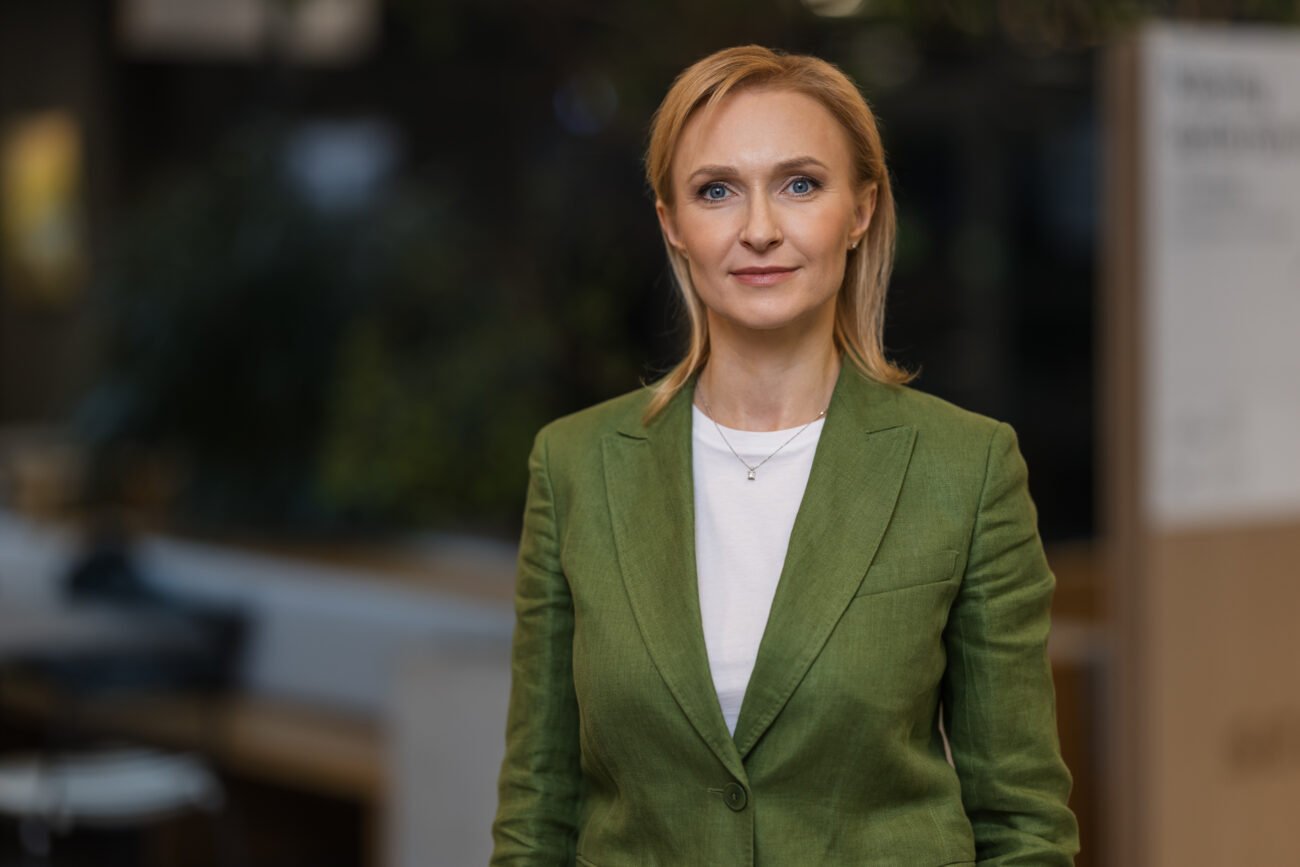 Verslo moteris žalia striuke stovi biuro aplinkoje