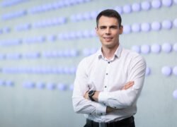 Susikryžiavęs rankas vyras stovi priešais abstraktų taškų raštą