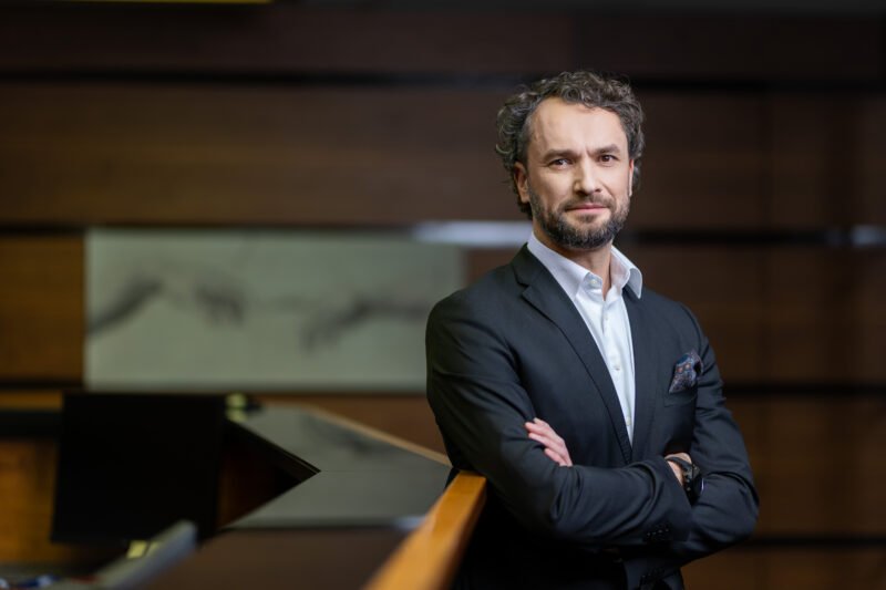 Verslo vyras su kostiumu stovi sukryžiavęs rankas moderniame interjere