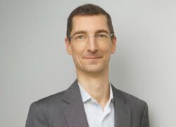 Verslo vyro portretas su akiniais ir pilku švarku pilkame fone