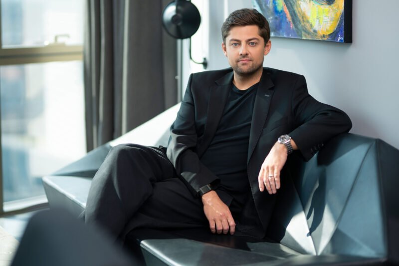 Vyras juodu kostiumu sėdi ant sofos moderniame interjere