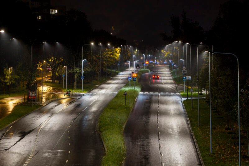 Lietingą naktį apšviesta Vilniaus gatvė su automobilių eismu