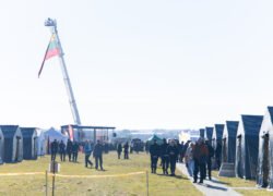 Palapinių miestelis ir žmonės atviroje aikštėje su iškelta vėliava