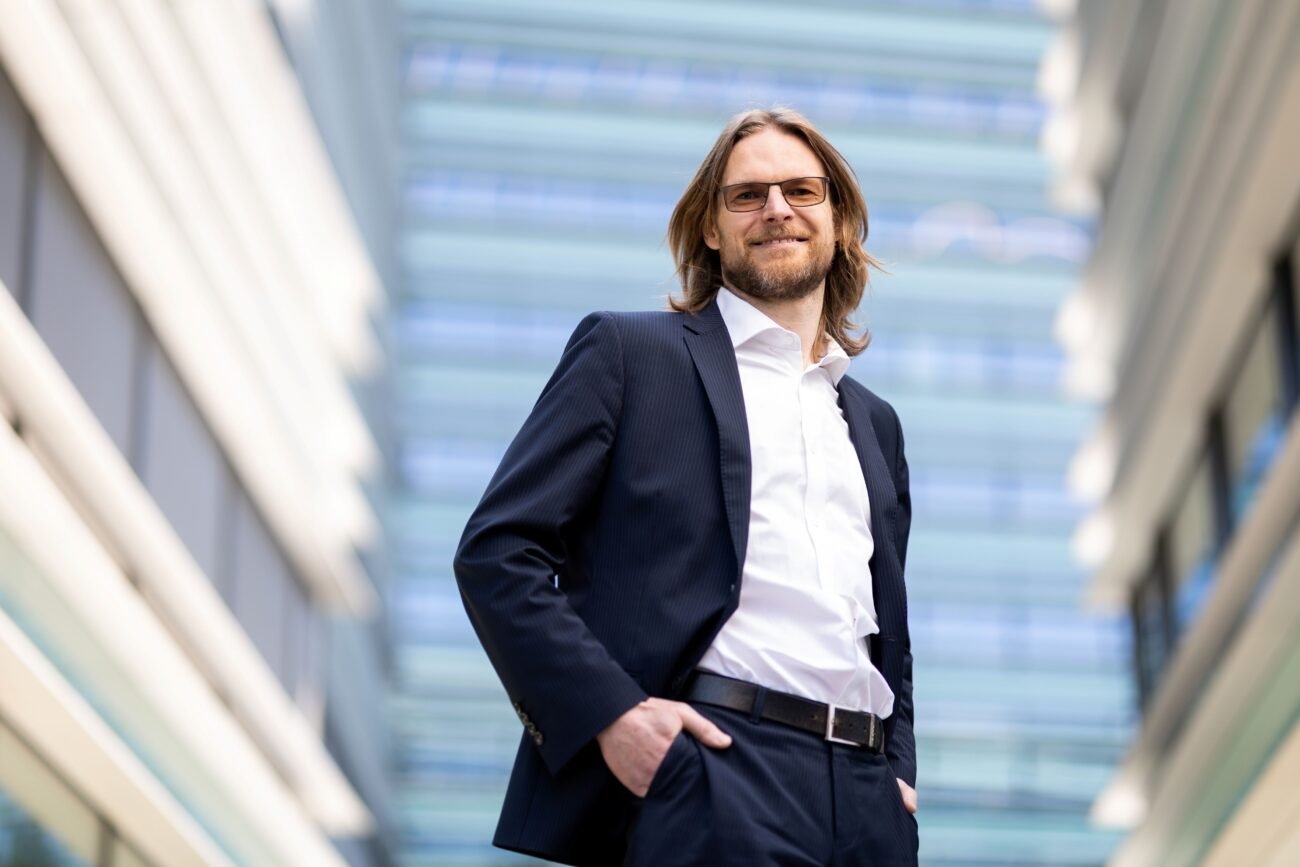 Kostiumu vilkintis vyras stovi tarp modernių stiklo pastatų