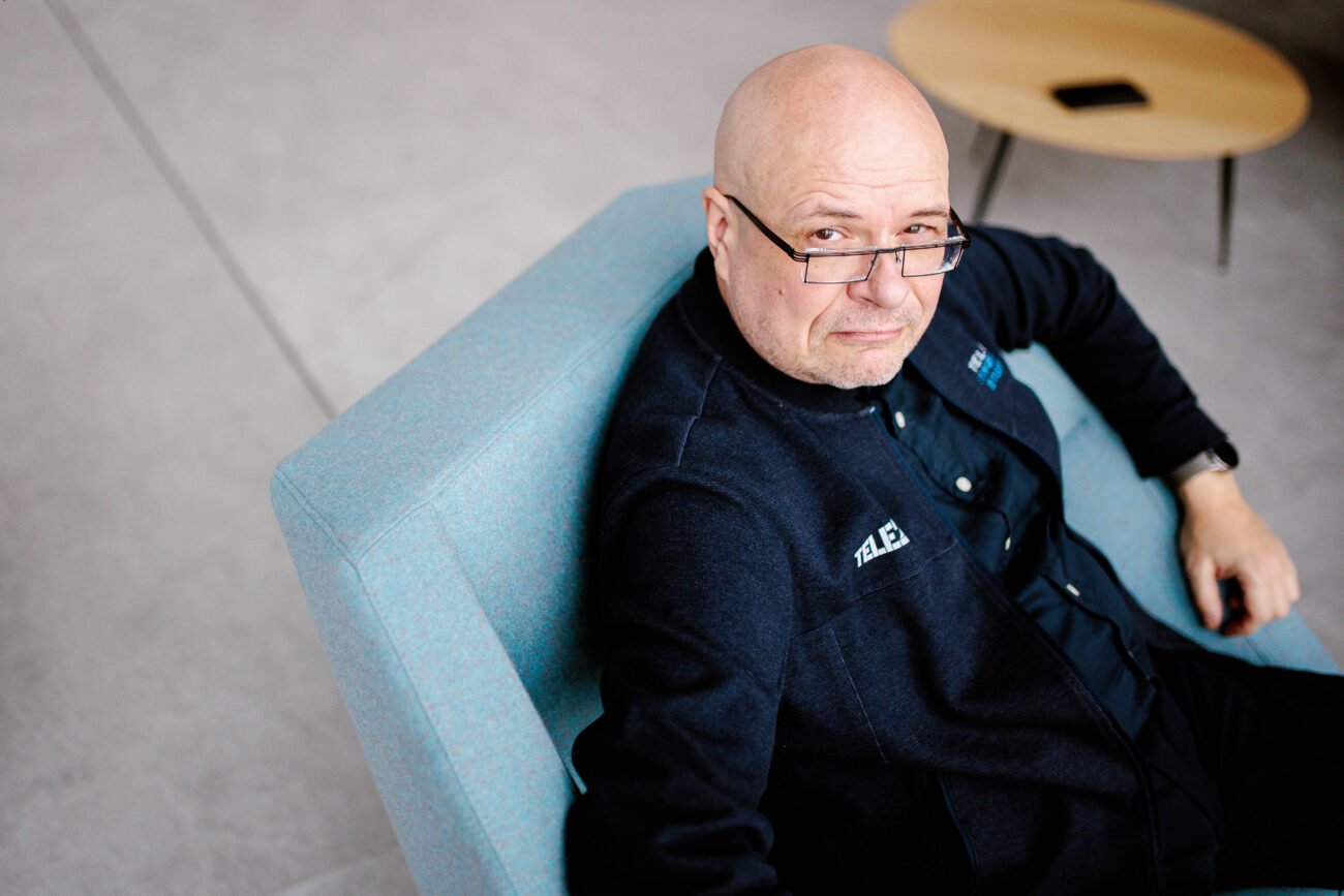 Vyras su akiniais sėdi mėlyname minkštasuolyje