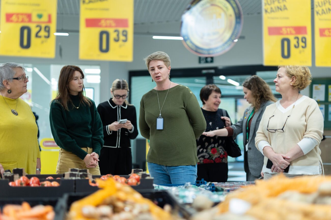 Žmonės stovi prekybos salėje prie geltonų akcijų kainų ženklų