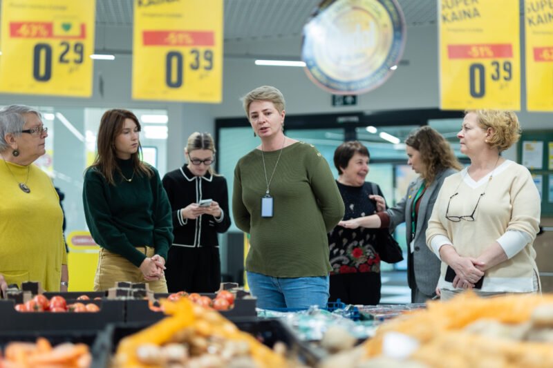 Žmonės stovi prekybos salėje prie geltonų akcijų kainų ženklų